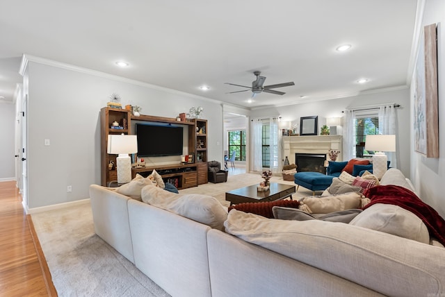 living area with ornamental molding, a fireplace with raised hearth, and a ceiling fan