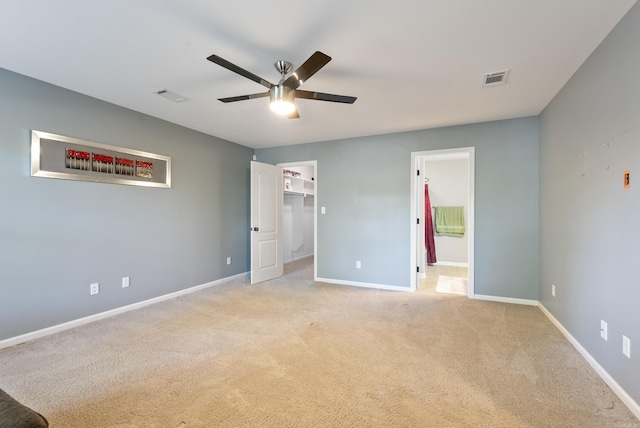unfurnished bedroom featuring visible vents, baseboards, a walk in closet, and light carpet