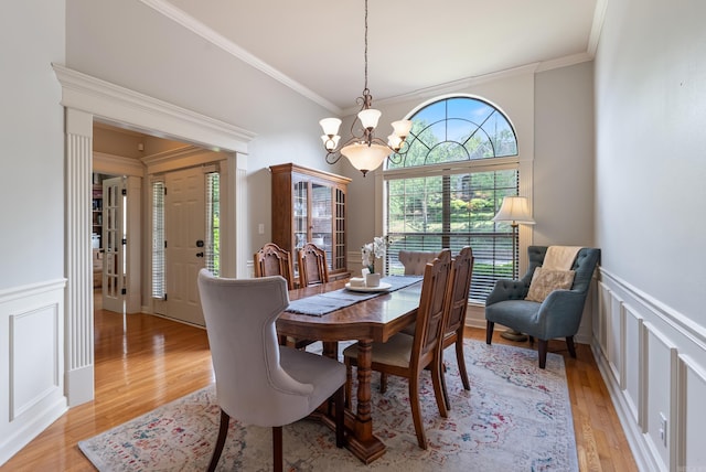 dining area with an inviting chandelier, ornamental molding, a decorative wall, and light wood-type flooring