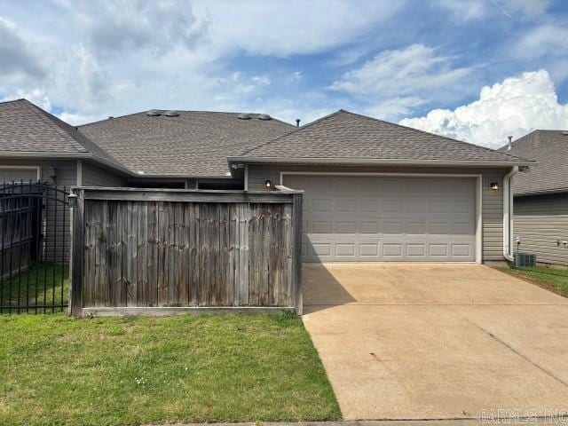 exterior space featuring driveway, roof with shingles, a front yard, an attached garage, and fence