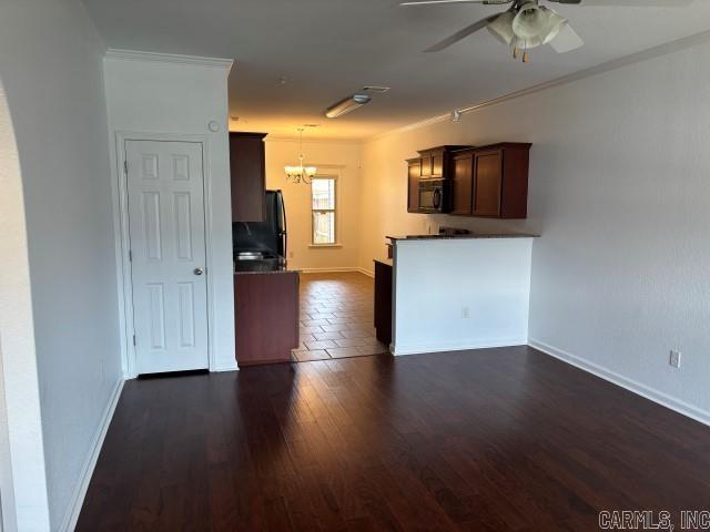 unfurnished living room featuring ornamental molding, dark wood-style flooring, baseboards, and ceiling fan with notable chandelier