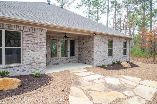 entrance to property with a patio, a ceiling fan, a shingled roof, and brick siding