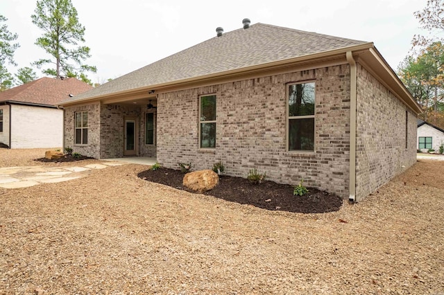 rear view of house featuring brick siding and roof with shingles