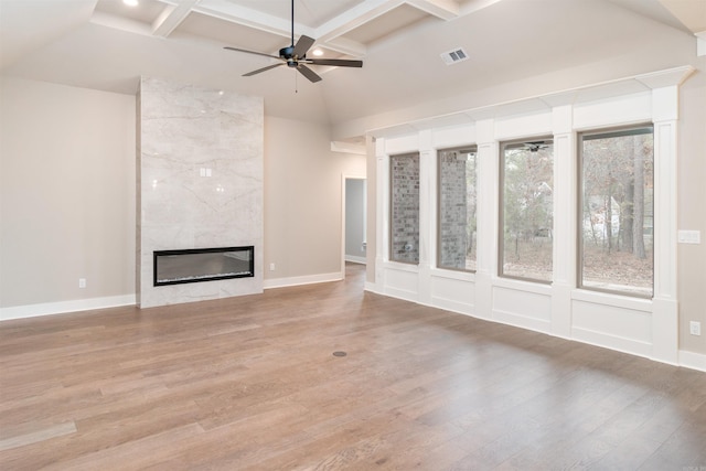 unfurnished living room featuring coffered ceiling, a high end fireplace, light wood finished floors, visible vents, and a ceiling fan