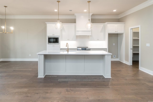 kitchen with built in microwave, ornamental molding, a kitchen island with sink, and white cabinets