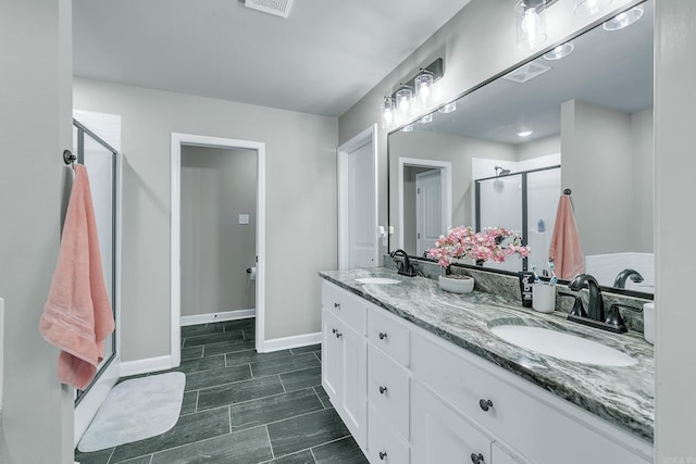 bathroom with double vanity, a shower stall, baseboards, and a sink