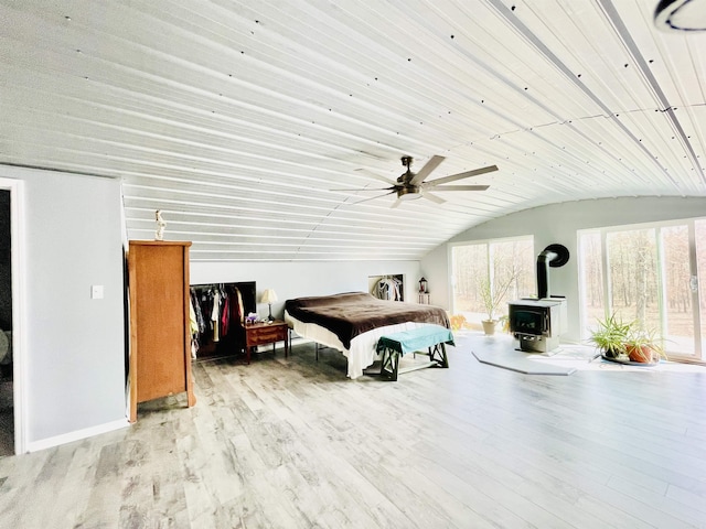 bedroom with baseboards, a wood stove, wood finished floors, and lofted ceiling