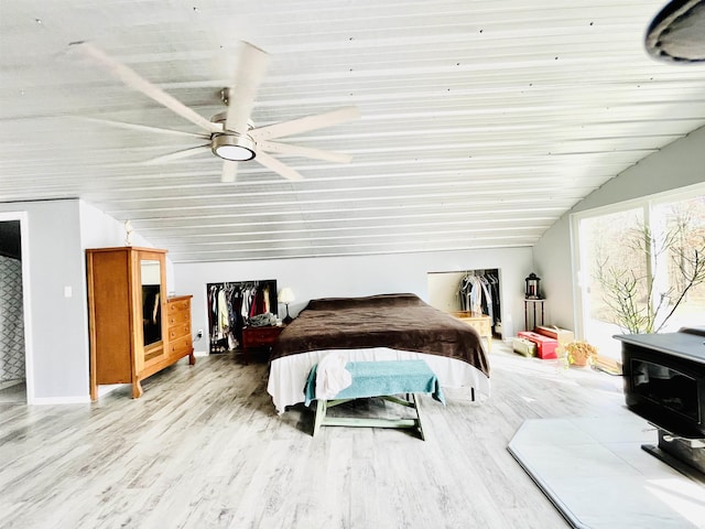 bedroom with a wood stove, a ceiling fan, vaulted ceiling, and wood finished floors