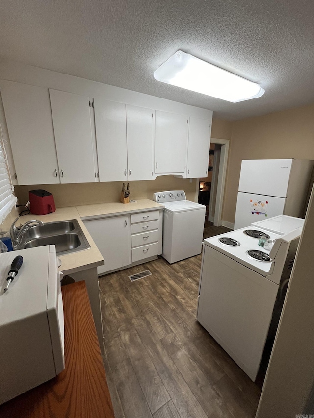kitchen featuring a sink, a textured ceiling, dark wood-type flooring, white appliances, and washer / clothes dryer