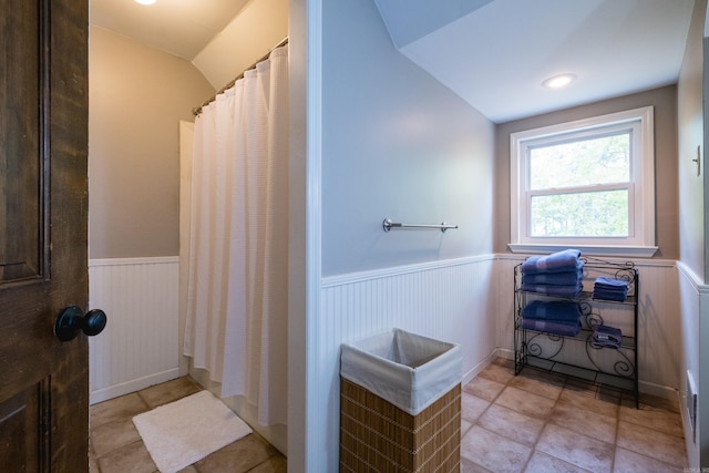 full bath featuring tile patterned floors, curtained shower, a wainscoted wall, and vaulted ceiling