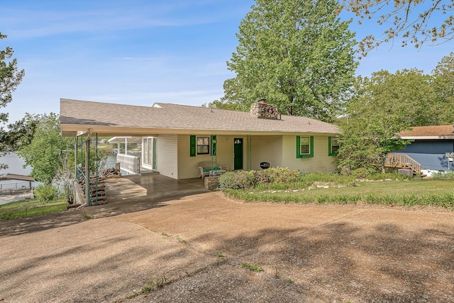 ranch-style house with a chimney, a porch, concrete driveway, and an attached carport