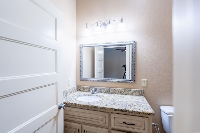 bathroom featuring toilet, a textured wall, and vanity