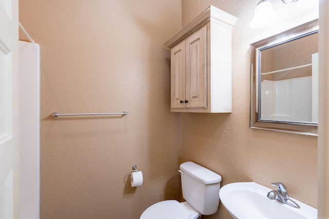 bathroom featuring a textured wall, toilet, and a sink