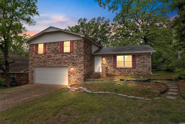tri-level home with a garage, brick siding, aphalt driveway, and a yard