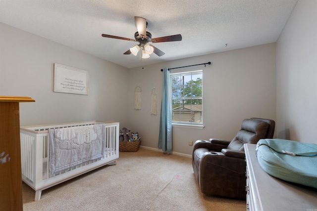 bedroom featuring a nursery area, carpet, baseboards, a ceiling fan, and a textured ceiling