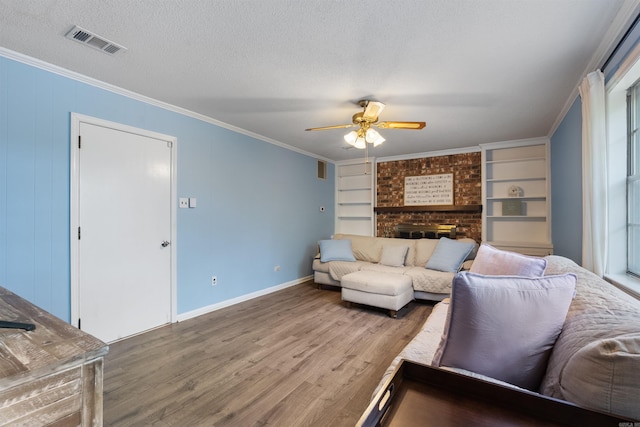 living area featuring crown molding, visible vents, ceiling fan, a brick fireplace, and wood finished floors