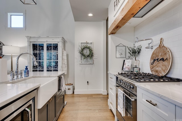 kitchen featuring light stone counters, decorative backsplash, a sink, appliances with stainless steel finishes, and light wood finished floors