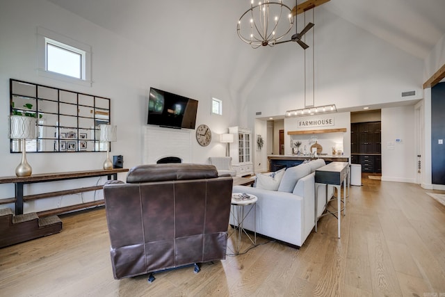 living area featuring visible vents, light wood-style flooring, a chandelier, a brick fireplace, and high vaulted ceiling