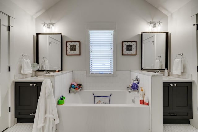 full bath with tile patterned floors, two vanities, vaulted ceiling, a bath, and a sink