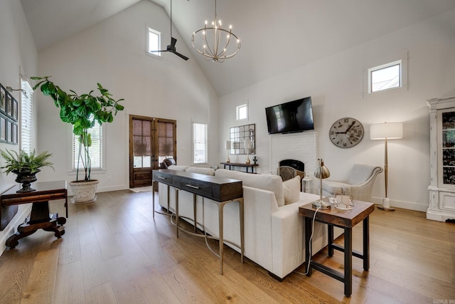 living area featuring high vaulted ceiling, light wood-style floors, a chandelier, and a healthy amount of sunlight