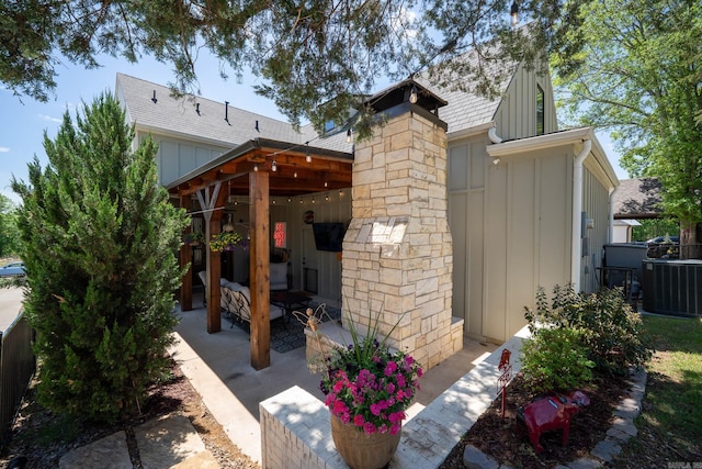 exterior space featuring cooling unit, board and batten siding, and roof with shingles