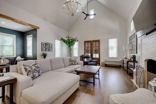 living room featuring high vaulted ceiling, an inviting chandelier, dark wood-type flooring, and a brick fireplace