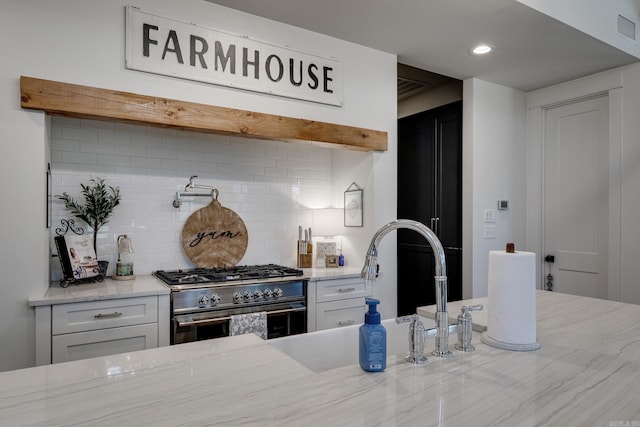 kitchen featuring high end stainless steel range oven, tasteful backsplash, white cabinets, light stone countertops, and recessed lighting