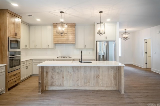 kitchen featuring a sink, a notable chandelier, light wood-style flooring, light countertops, and appliances with stainless steel finishes