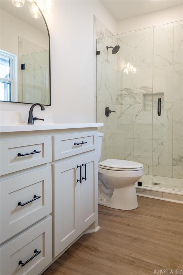 full bath featuring wood finished floors, a marble finish shower, toilet, and vanity