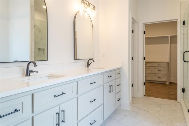 bathroom with marble finish floor, a sink, double vanity, and a spacious closet