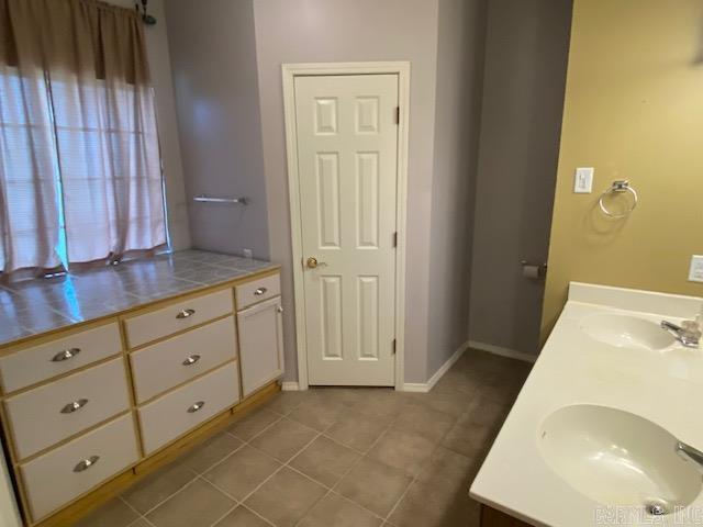 bathroom featuring tile patterned floors, baseboards, double vanity, and a sink