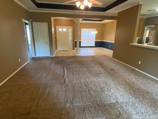 unfurnished living room featuring carpet floors, baseboards, ornamental molding, and ceiling fan with notable chandelier