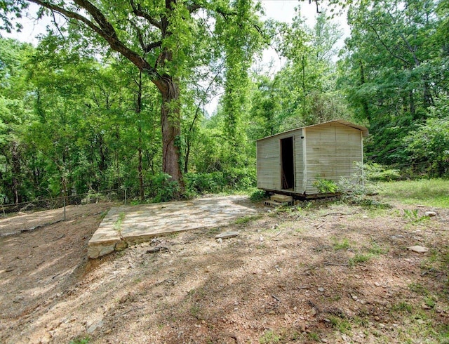 view of yard with fence, an outbuilding, a forest view, and a storage shed