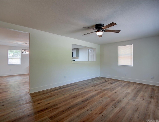 spare room featuring baseboards, wood finished floors, and ceiling fan with notable chandelier
