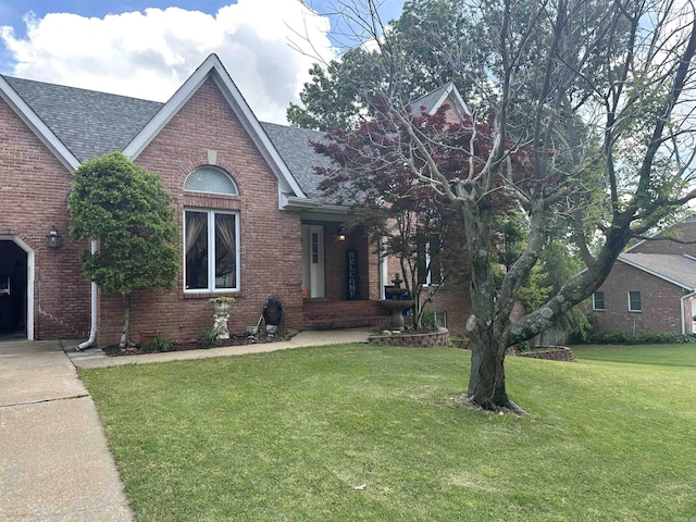 view of front facade featuring roof with shingles, a front lawn, and brick siding