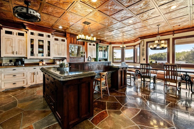 kitchen featuring crown molding, a kitchen island with sink, a notable chandelier, and glass insert cabinets