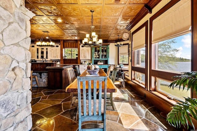 dining space with a chandelier, a water view, stone finish flooring, an ornate ceiling, and crown molding