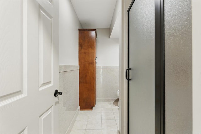 bathroom with toilet, tile walls, tile patterned flooring, and a stall shower