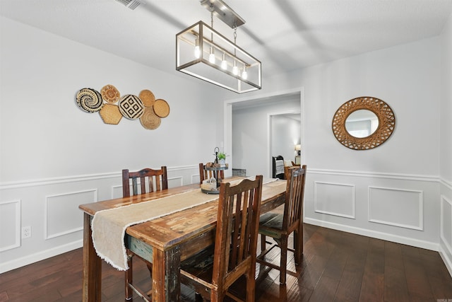 dining room with a wainscoted wall, a decorative wall, a chandelier, and dark wood-type flooring