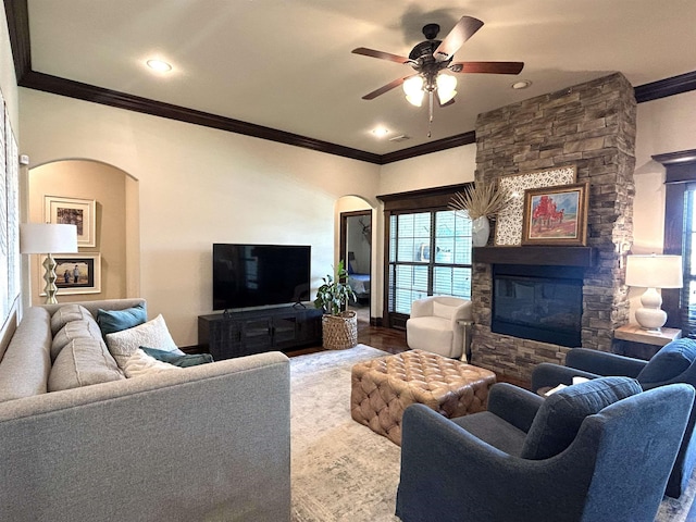 living room with crown molding, arched walkways, ceiling fan, and a fireplace