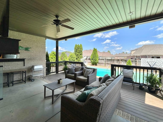 deck with grilling area, an outdoor living space, a ceiling fan, a fenced in pool, and a fenced backyard