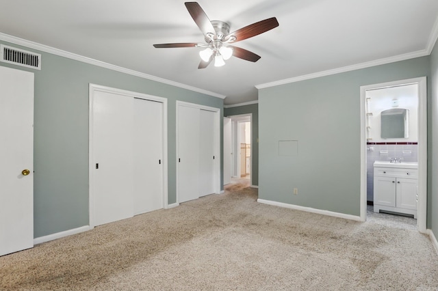 unfurnished bedroom featuring carpet flooring, visible vents, ensuite bathroom, ornamental molding, and two closets