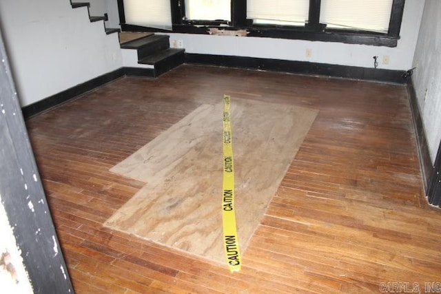 unfurnished room with wood-type flooring, stairway, and baseboards
