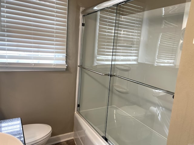 bathroom featuring baseboards, shower / bath combination with glass door, toilet, and a sink