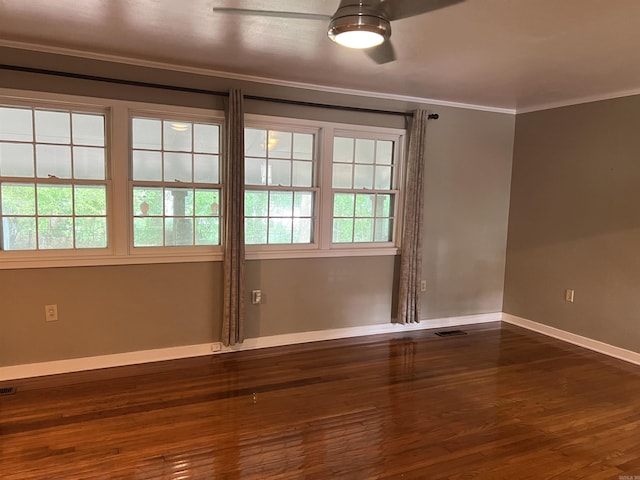 empty room with dark wood-style flooring, crown molding, a ceiling fan, visible vents, and baseboards