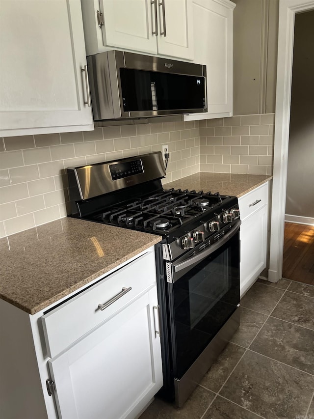 kitchen featuring appliances with stainless steel finishes, white cabinetry, dark stone countertops, and backsplash