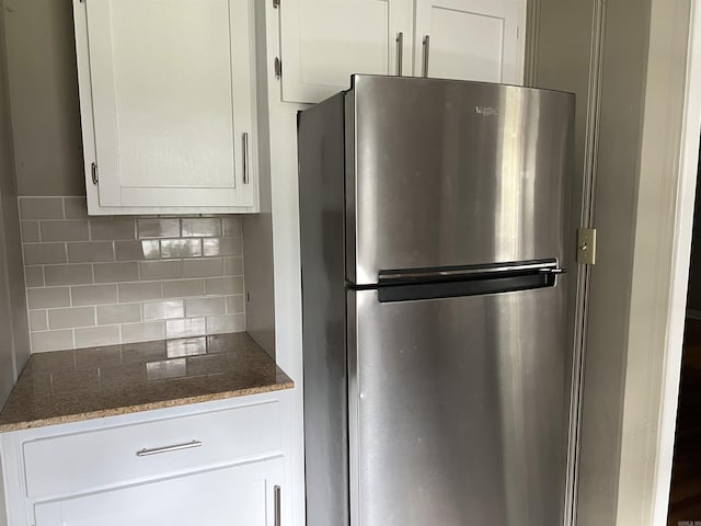 kitchen with dark stone countertops, white cabinets, decorative backsplash, and freestanding refrigerator
