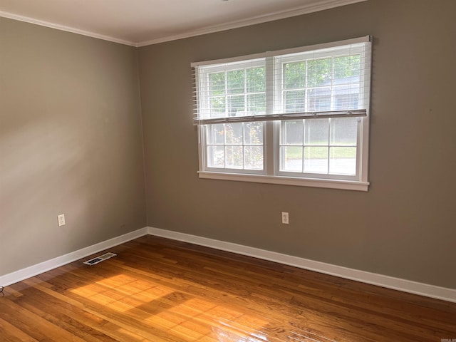 empty room featuring ornamental molding, visible vents, wood finished floors, and baseboards