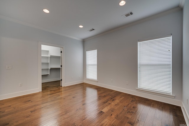 empty room with baseboards, ornamental molding, hardwood / wood-style flooring, and visible vents