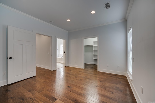 unfurnished bedroom with visible vents, ornamental molding, a spacious closet, and hardwood / wood-style floors